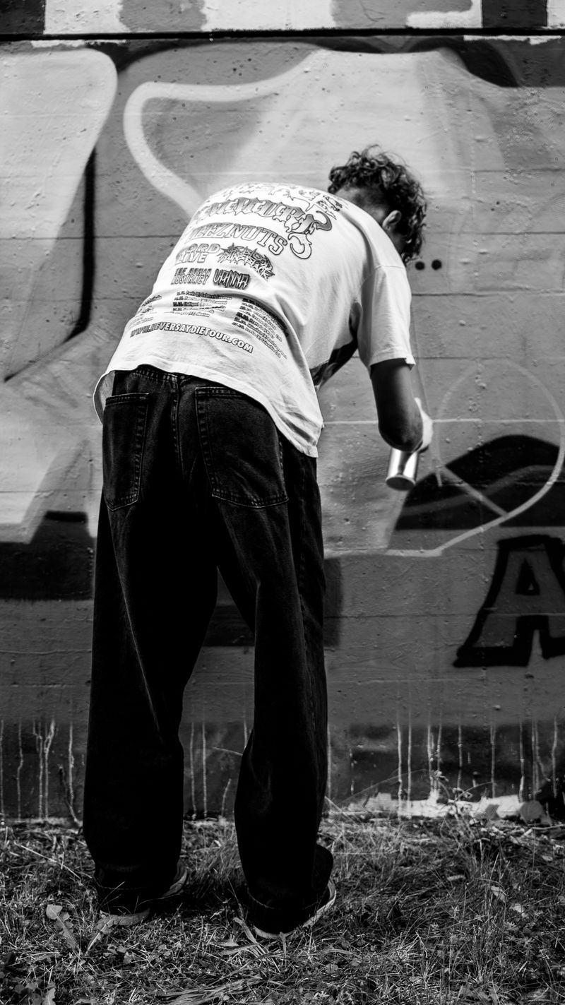 Street artist crouching and spray painting graffiti on a wall in black and white