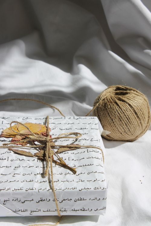 Free A unique handmade gift box wrapped in script paper, adorned with dried leaves and twine, on white fabric. Stock Photo