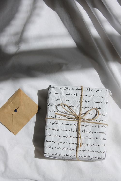 Free A uniquely wrapped gift with scripted paper and twine, accompanied by a heart-sealed envelope on a fabric background. Stock Photo