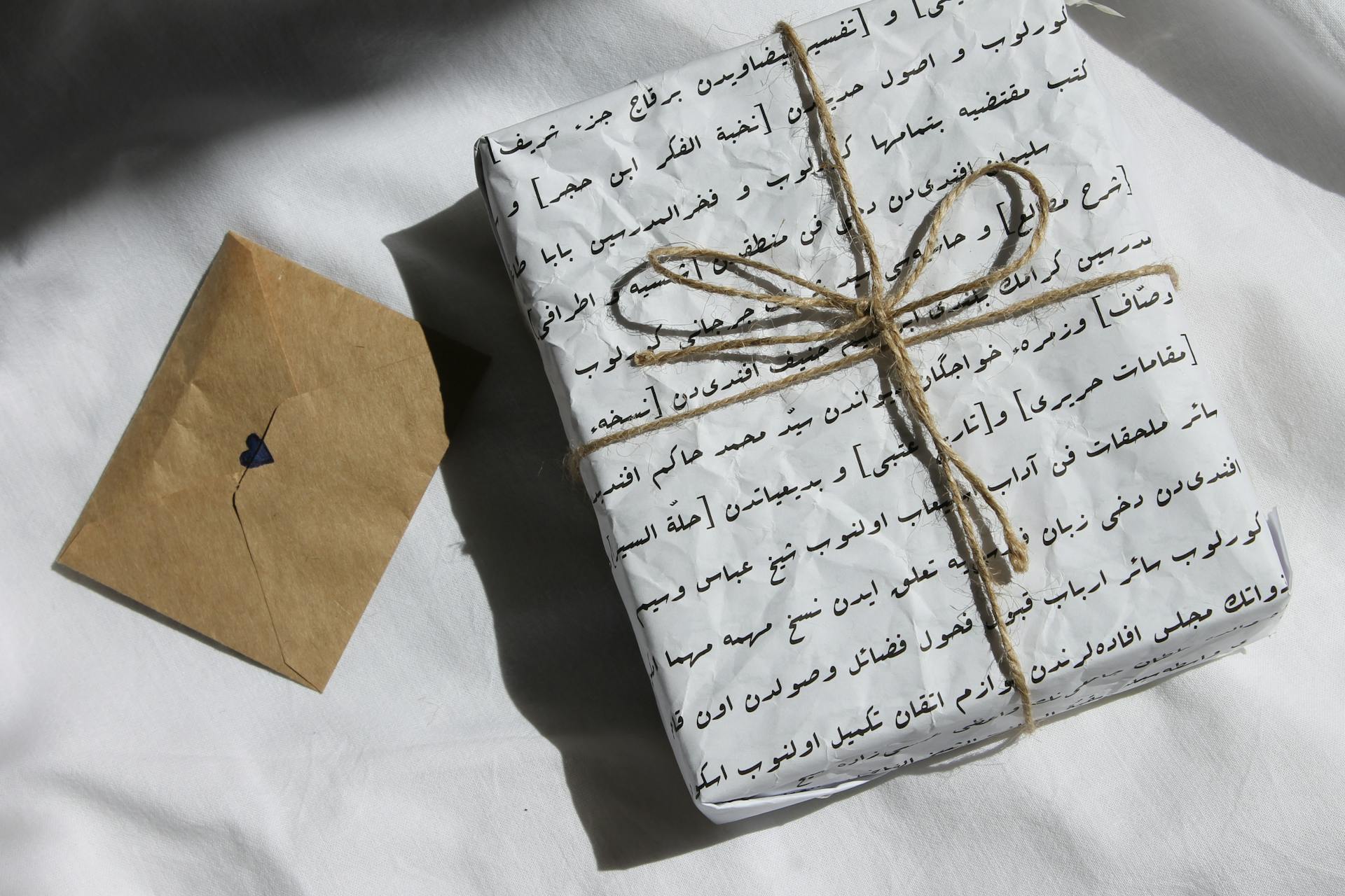 A Gift Box Wrapped with White Cover Beside a Brown Envelope