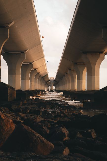 Dynamic view of bridge columns spanning over a rocky riverbank under a cloudy sky.