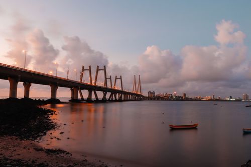 Free A breathtaking evening view of a bridge extending over calm waters, with city skyline in the background. Stock Photo