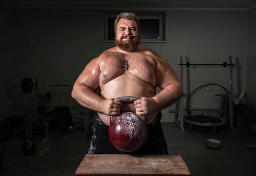 Muscular man lifting heavy kettlebell in gym, showcasing strength and fitness.