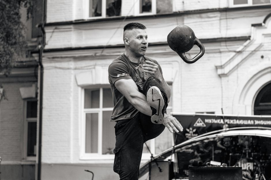 Man performing kettlebell trick in city street displaying strength and skill.