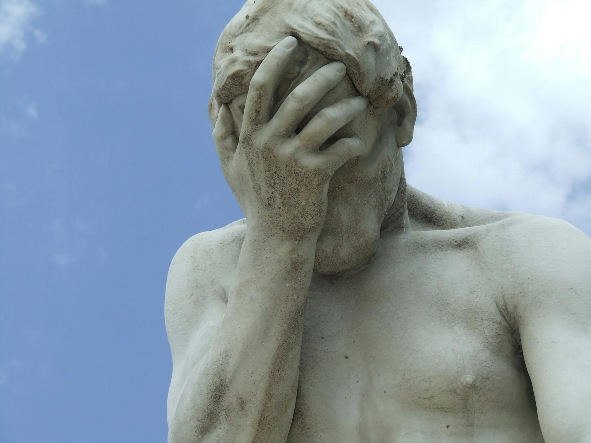 Statue of a man with blue sky behind holding his head in his hand