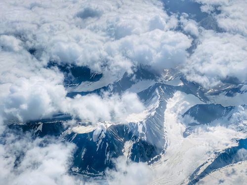 Free Stunning aerial photograph of snow-covered mountains peeking through clouds. Stock Photo