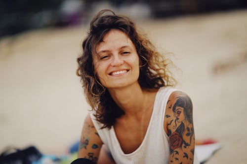 A Tattooed Woman Wearing White Tank Top while Smiling at the Camera