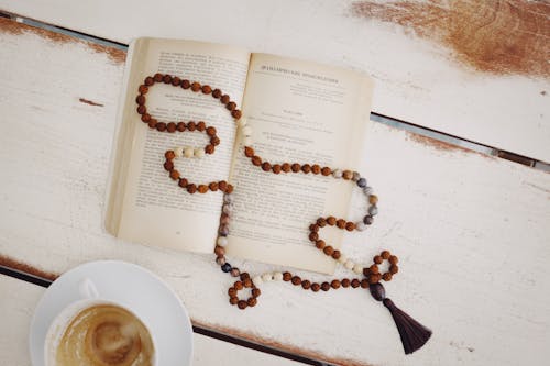 Free An Open Book with Beaded Necklace on Top Near a Cup of Coffee  Stock Photo