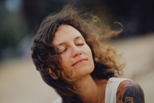 Free Close-up of a woman with eyes closed, enjoying the wind, with a tattoo visible on her shoulder. Stock Photo