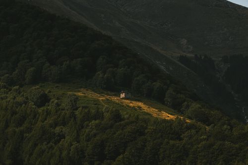 Free A serene aerial view of a lone cabin nestled among lush green hills and mountains. Stock Photo