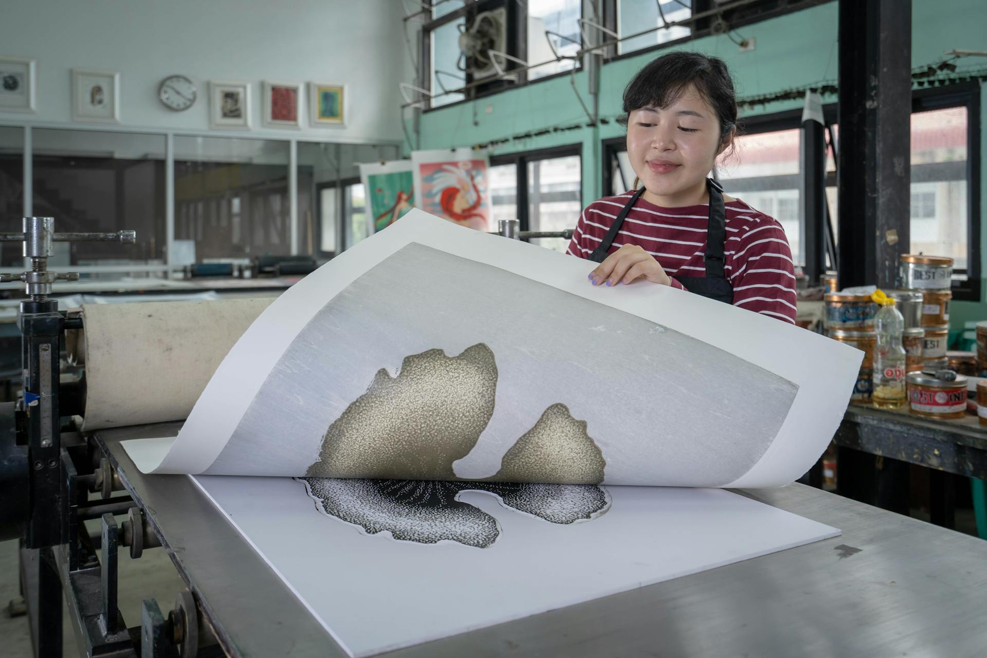 Asian woman artist working in a printmaking studio with a printing press. Creativity in action.