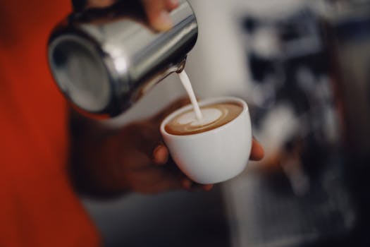 Close-up of a barista pouring steamed milk to create latte art in a coffee cup.