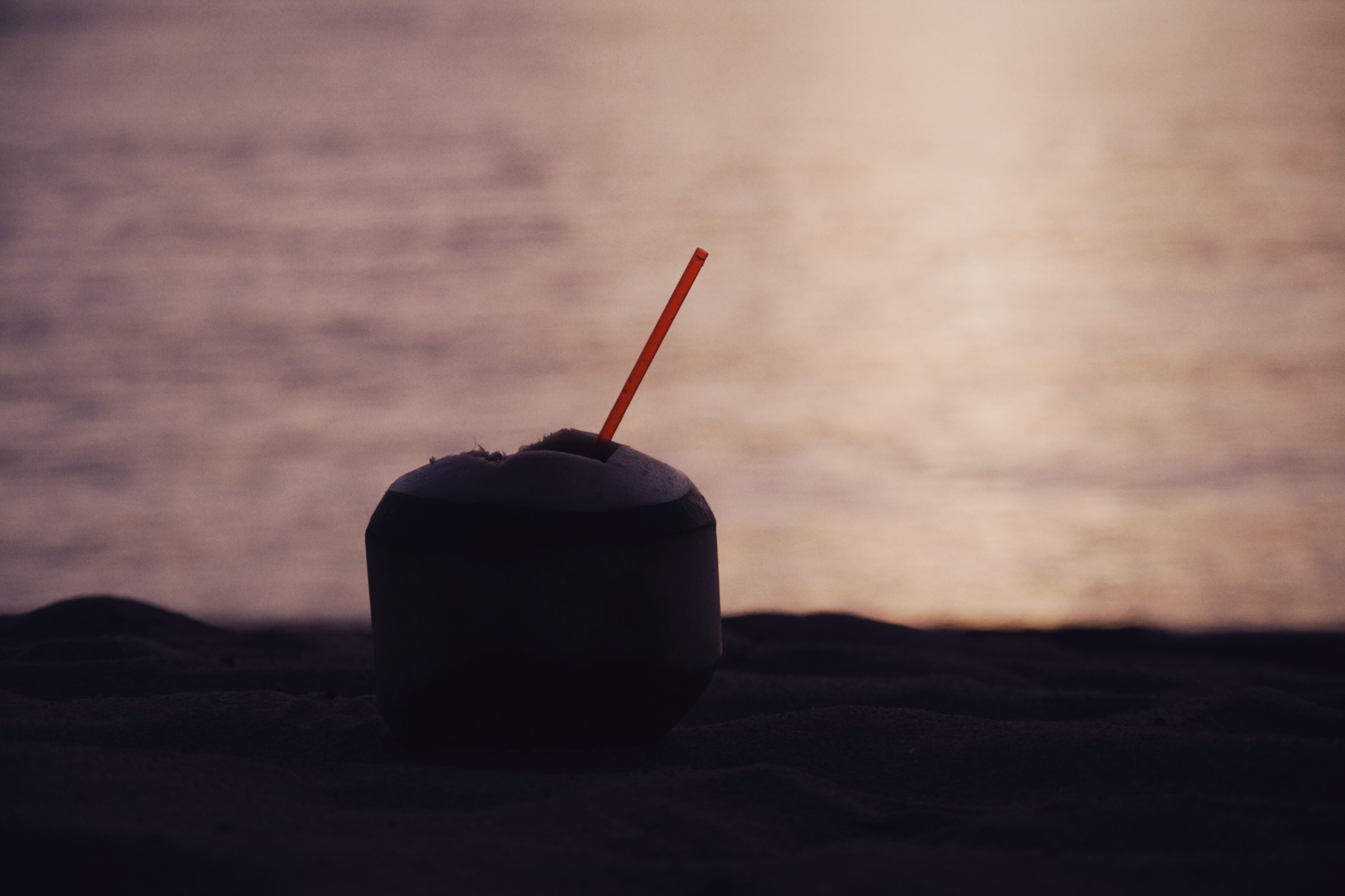 Fresh coconut with a straw resting on golden beach sand at sunset