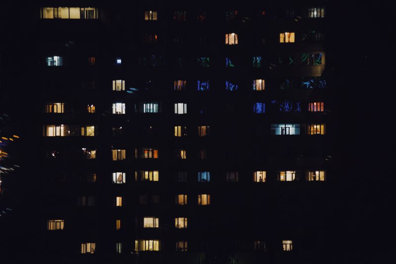 Lit windows across a residential apartment block at night — photo by Alexey Demidov on Pexels