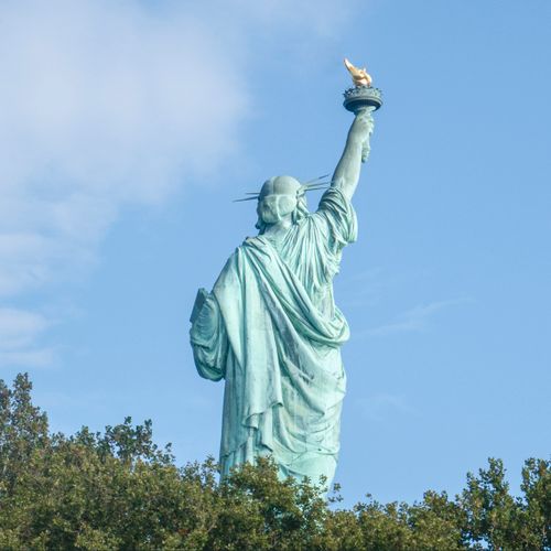 Free Back view of the iconic Statue of Liberty with clear blue sky and trees, New York landmark. Stock Photo