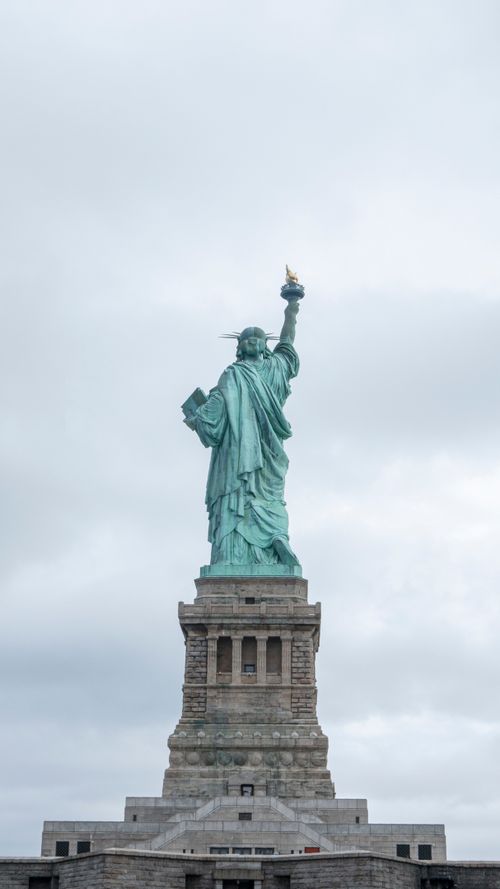 Free Rear view of the Statue of Liberty against a cloudy sky in New York City. Stock Photo