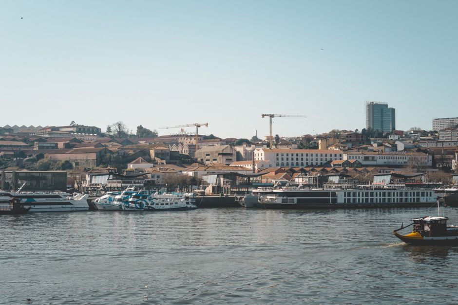Traditional Rabelo boats on the Douro River passing under a bridge in Porto, Portugal.