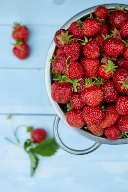 Free Close-up of ripe strawberries in a metal colander on a blue wooden table, showcasing vibrant colors and freshness. Stock Photo
