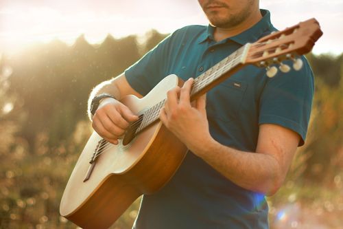 Free Adult man playing acoustic guitar outside with sunlight and a blurred background. Stock Photo