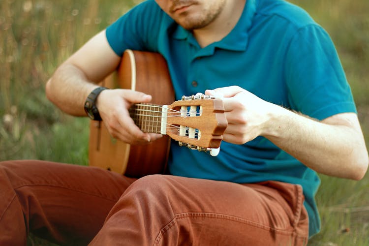 Man Sitting In Grass Playing Guitar