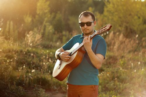Free Man playing guitar outdoors with sunlight glow, creating a warm and musical ambiance. Stock Photo