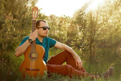Man Sitting on the Grass while Holding His Acoustic Guitar
