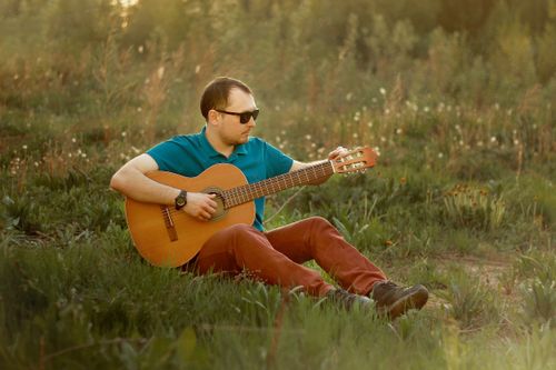 Free Adult man playing guitar outdoors in a meadow, wearing sunglasses and a turquoise shirt Stock Photo