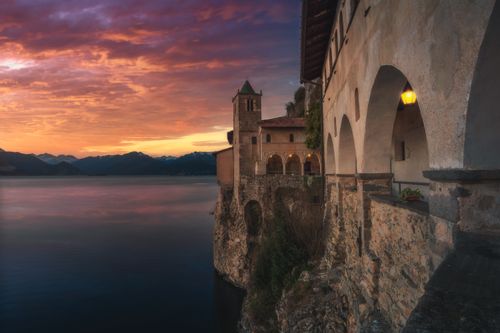 Free Scenic view of a historic monastery perched on a cliff overlooking Lake Maggiore at sunset in Italy. Stock Photo