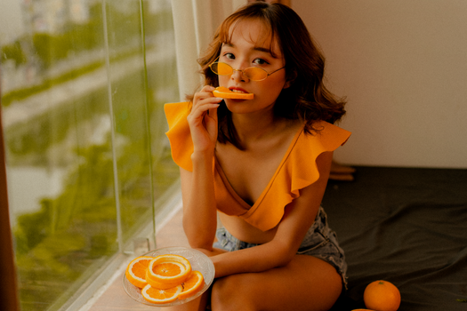 Young woman posing with oranges in bright, colorful setting, perfect for summer lifestyle content.