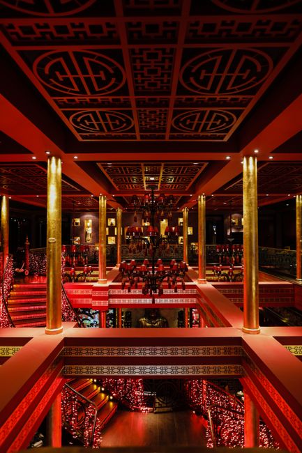 A luxurious Chinese-themed interior with ornate designs, chandeliers, pillars, and warm lighting.