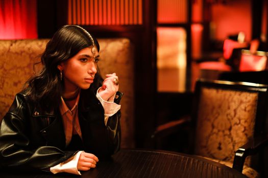 Woman in Leather Jacket Sitting on a Chair Leaning by the Wooden Table while Looking Afar