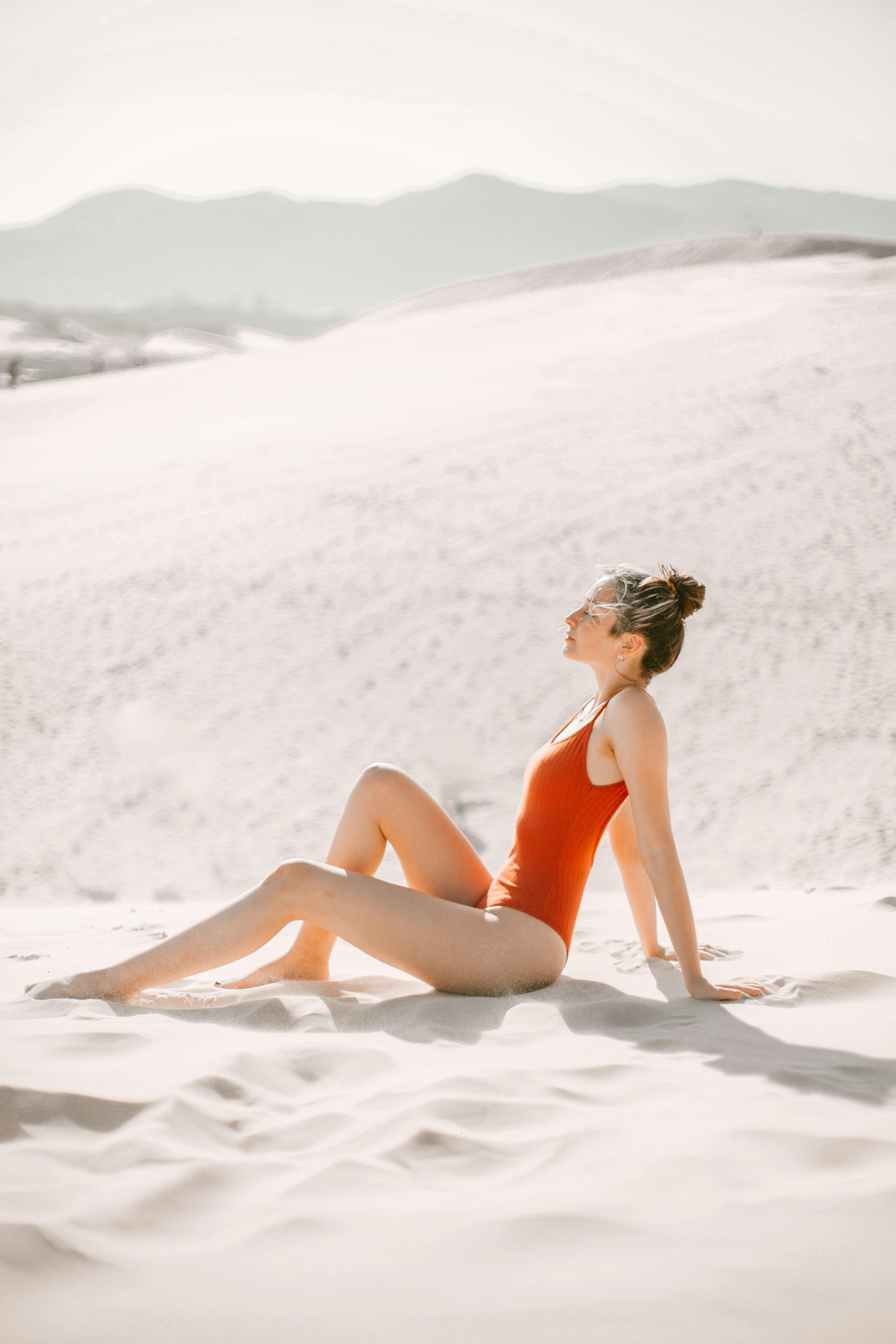 Woman in red swimsuit enjoying sun on a sand dune in summer
