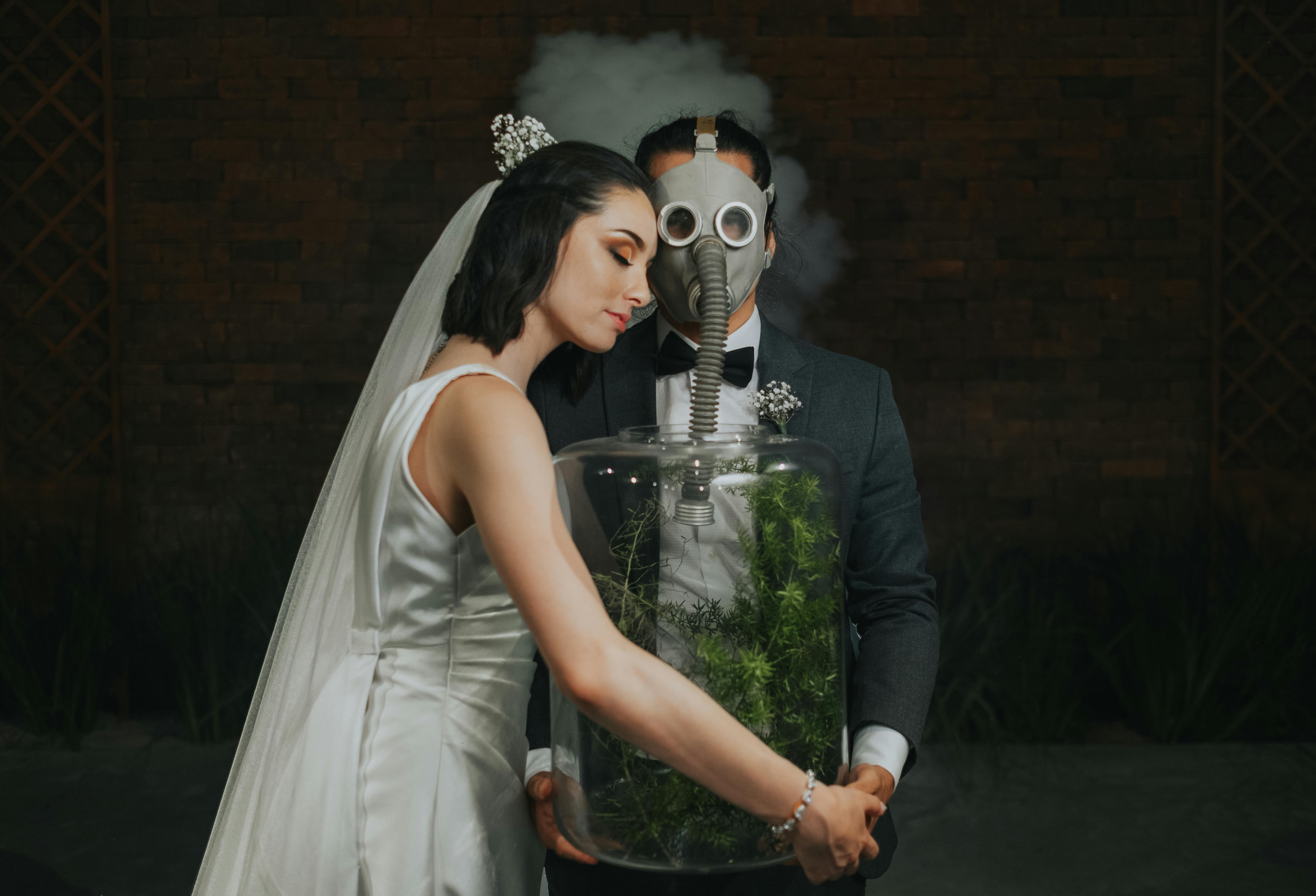 A creative wedding photo featuring a bride and groom in a studio with a gas mask and glass jar.