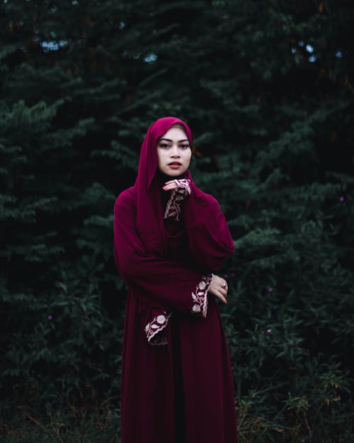 A Woman in Red Abaya Standing while Looking at the Camera
