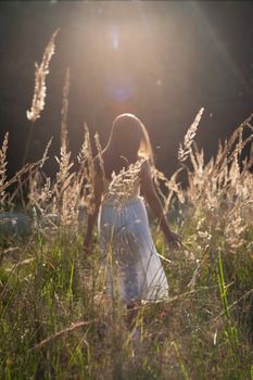 A back view of a woman in a white dress walking through a wheat field at sunset.