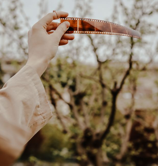 A woman's hand holding a vintage film strip outdoors with trees in the background during spring.