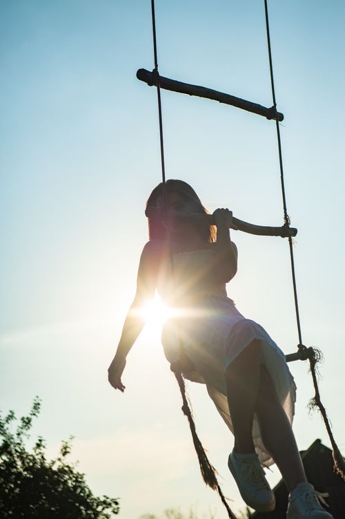 Free A woman climbs a rope ladder outdoors, silhouetted against a sunset backdrop, capturing a moment of balance and adventure. Stock Photo