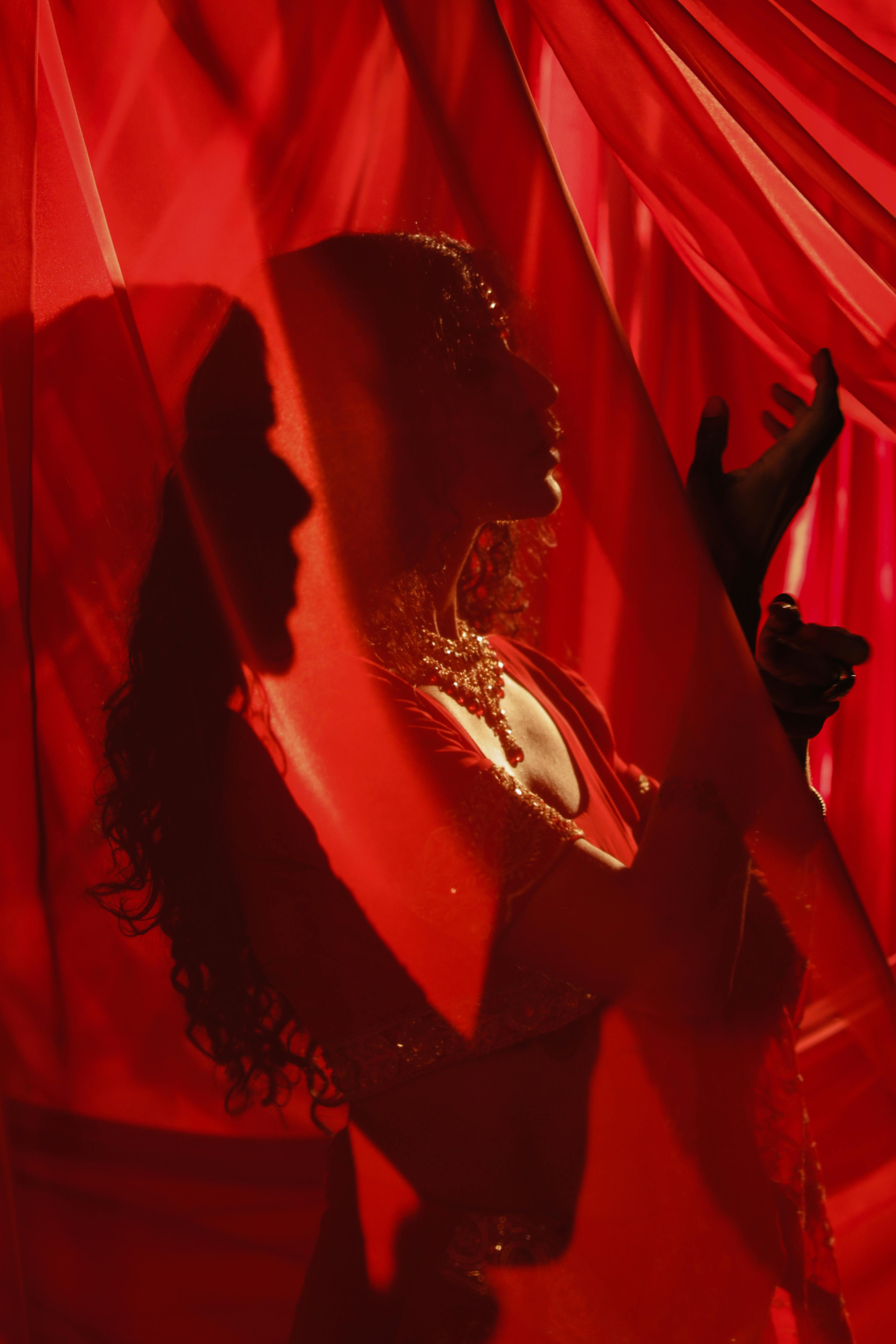 Free Artistic silhouette of a woman framed by vibrant red curtains exuding elegance and mystery. Stock Photo