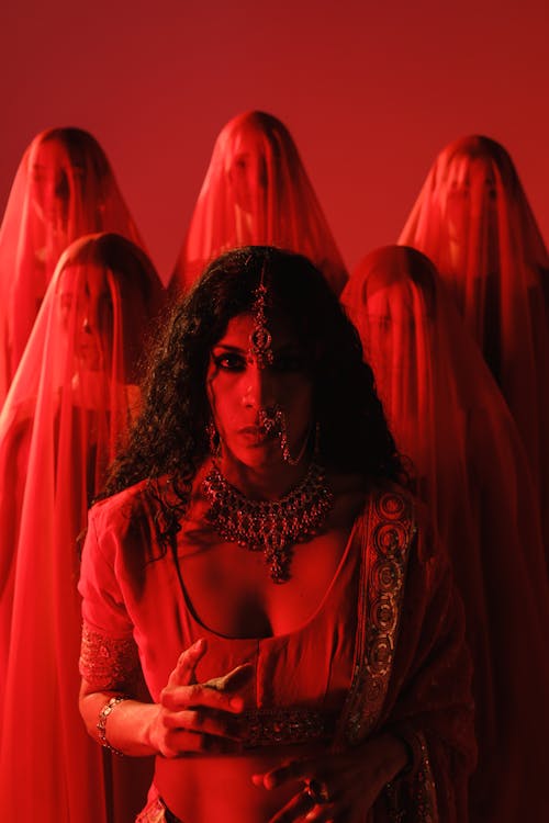 Brunette in Traditional Jewelry and Sari Standing in front of Women in Veils