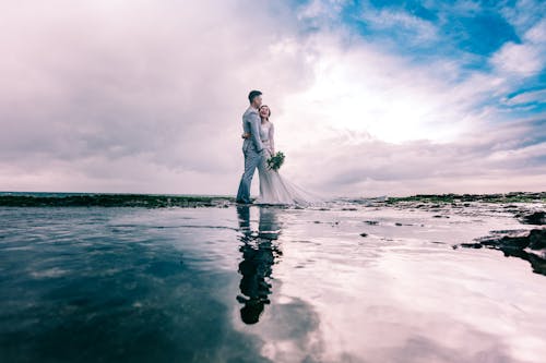 Free Man in Gray Dress Suit Jacket Embraces Woman Wearing Wedding Gown Stock Photo