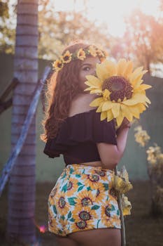 A woman wearing sunflower print shorts and flower crown holds a sunflower outdoors.