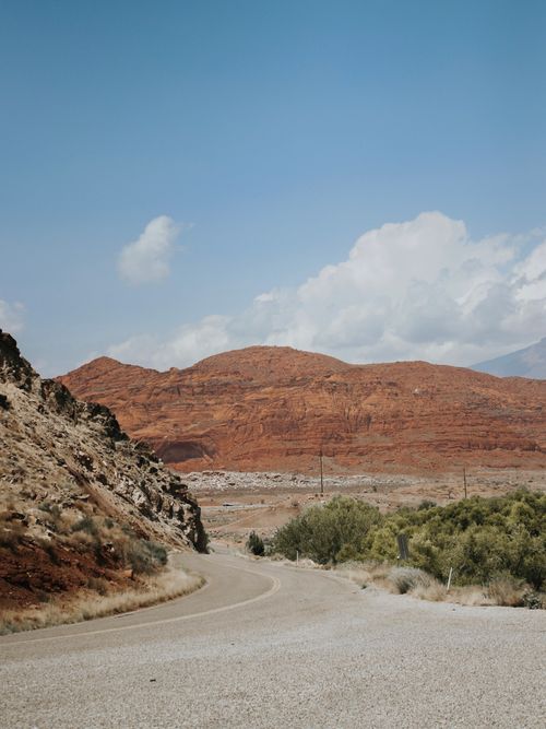 Free A winding road through a desert landscape with red rock hills under a blue sky and clouds. Stock Photo