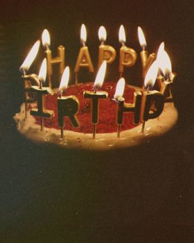 A festive birthday cake with illuminated candles spelling out 'Happy Birthday' atop a frosted surface.