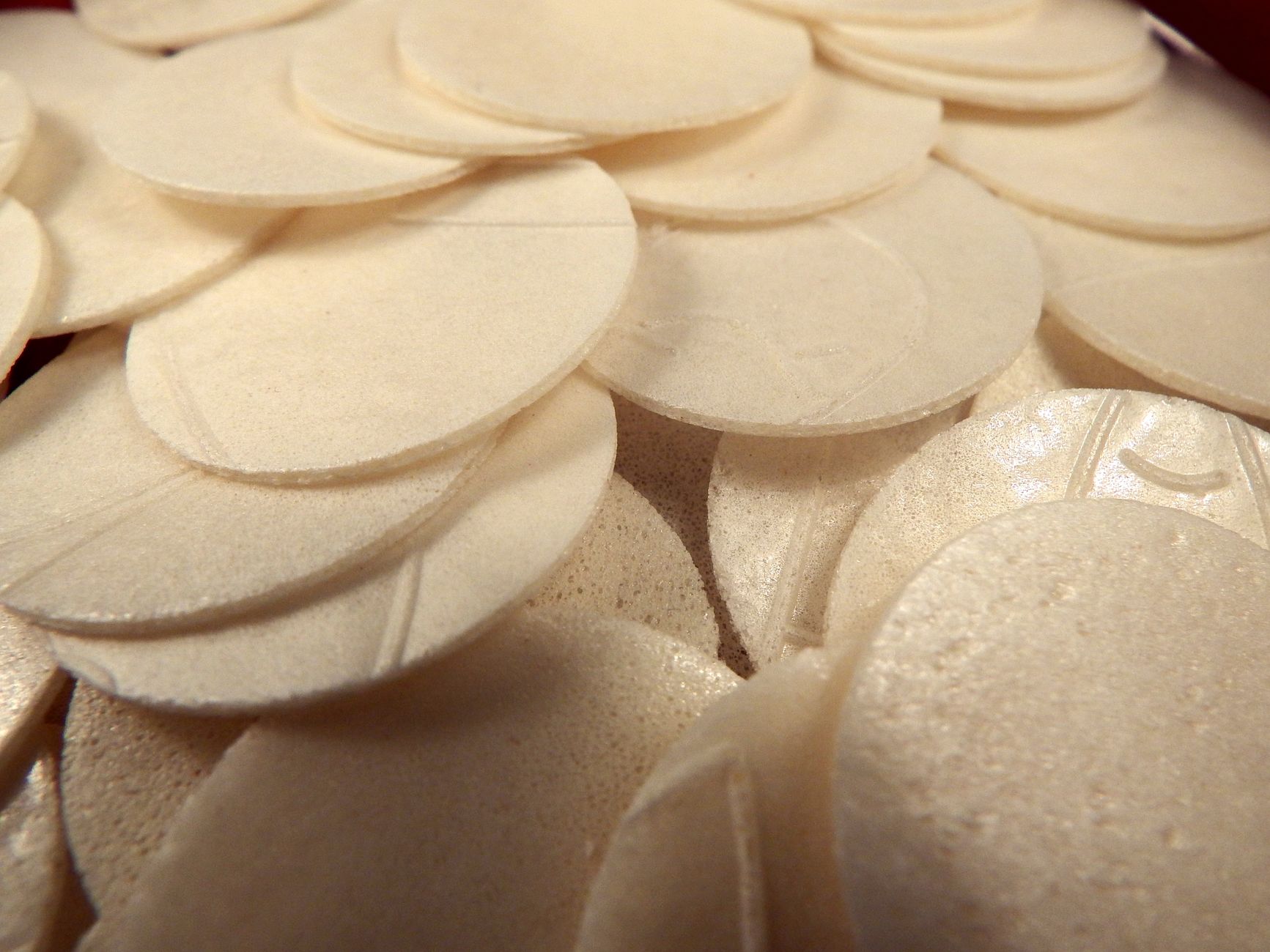 High angle closeup of many thin white Communion bread hosts used in Christian ritual of Eucharist