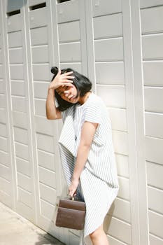 Elegant woman in a pinstripe dress poses against a bright outdoor backdrop, holding a handbag.