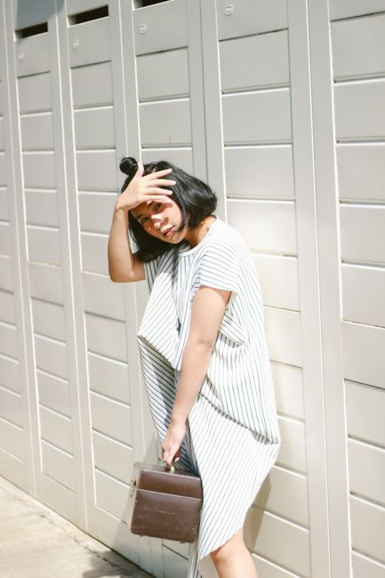 Elegant woman in a pinstripe dress poses against a bright outdoor backdrop, holding a handbag.