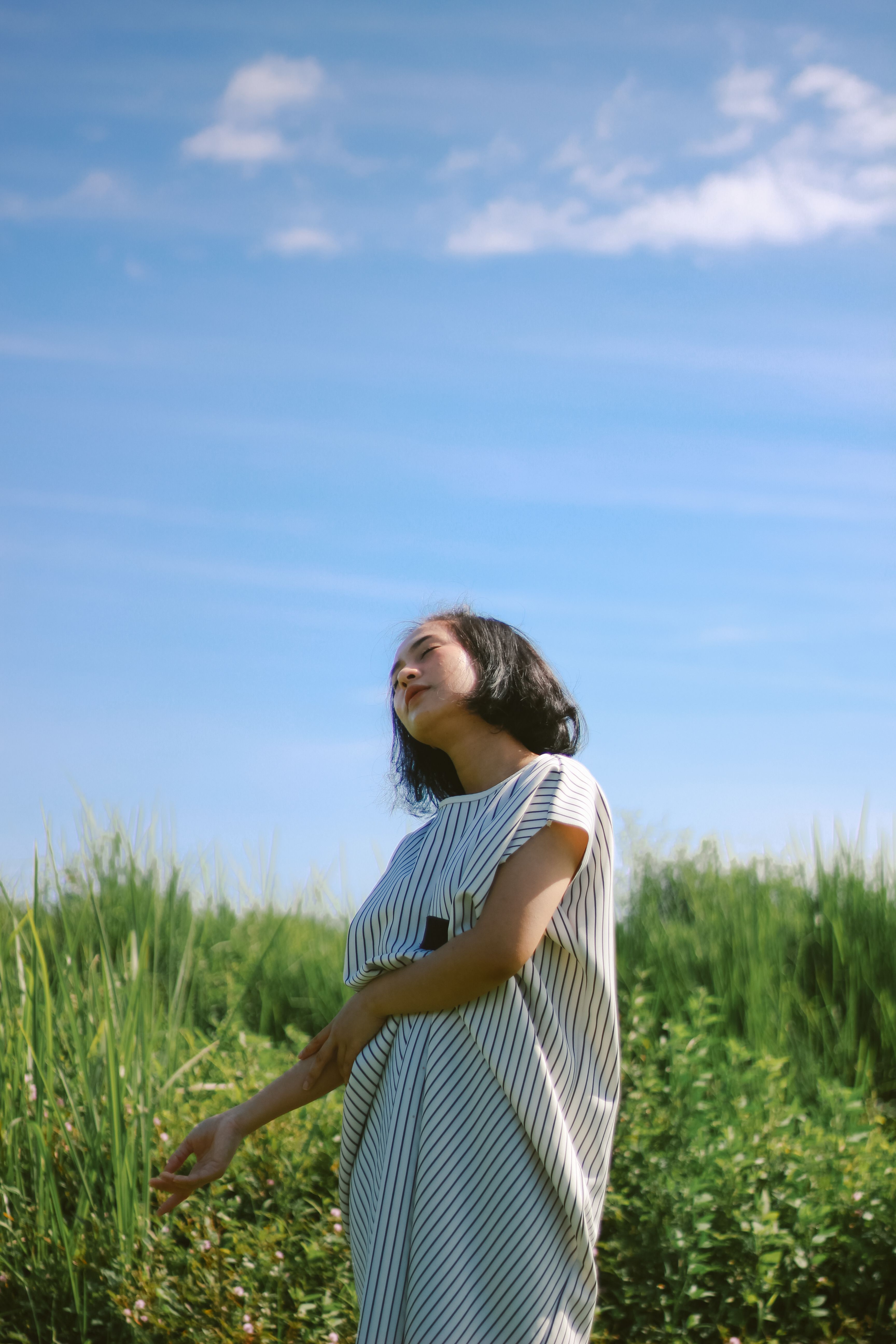 Woman outdoors with eyes closed, appearing calm and relaxed under open sky