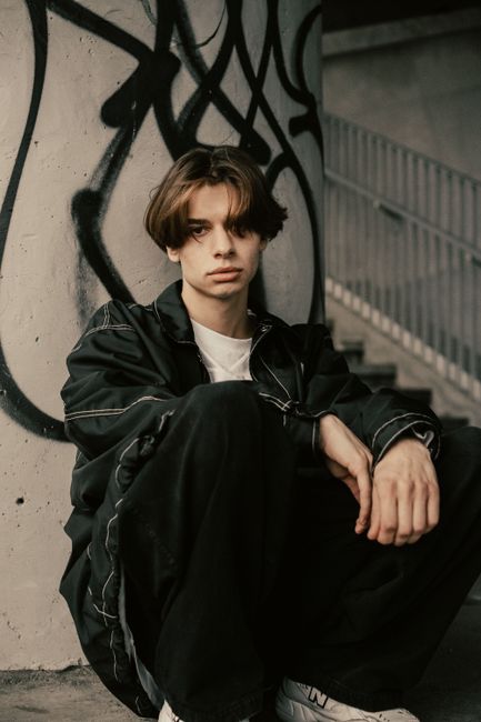 Moody portrait of a teenage boy sitting on a graffiti-covered staircase.