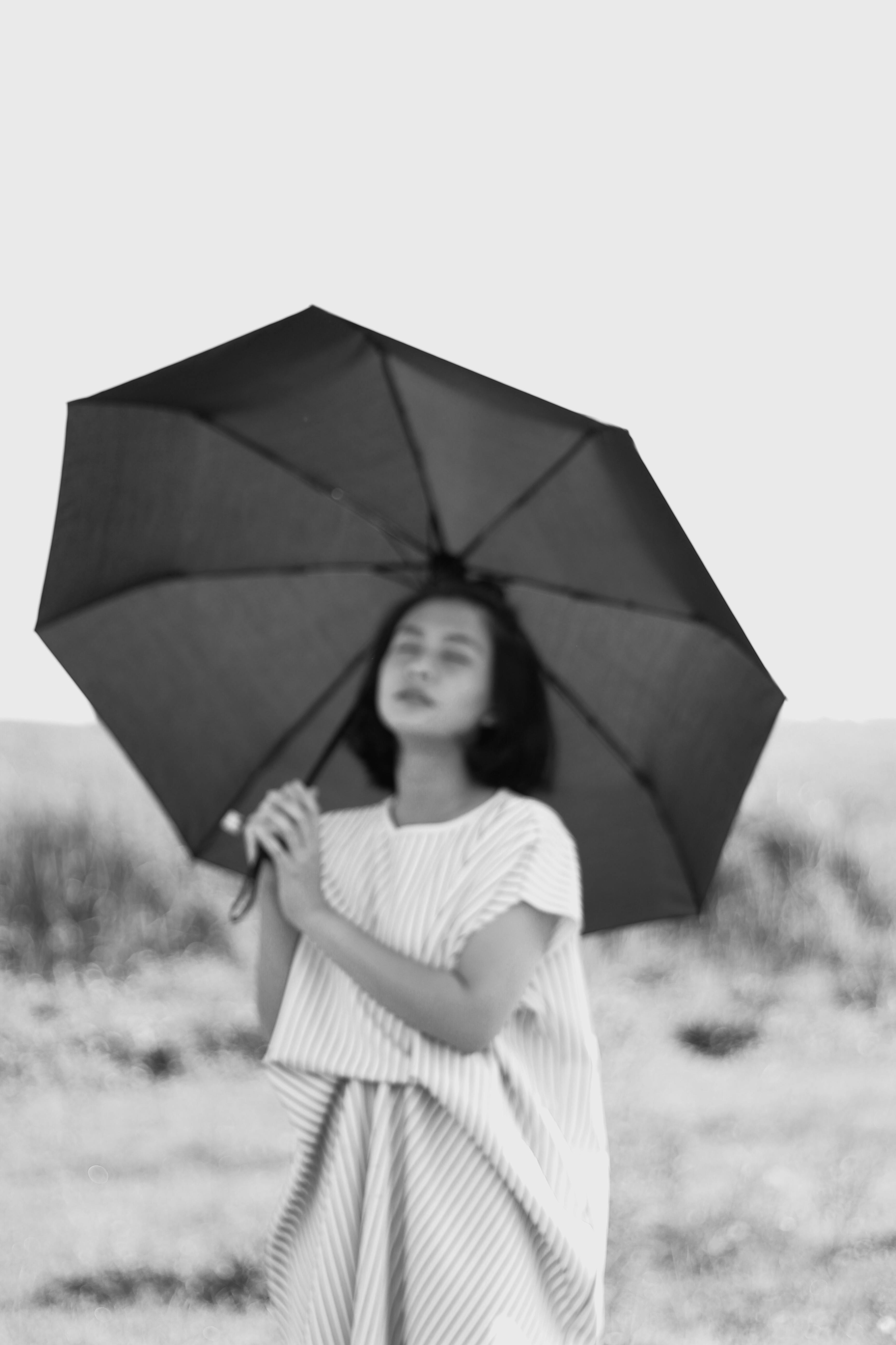 Blurry monochrome photo of a woman holding an umbrella outdoors.