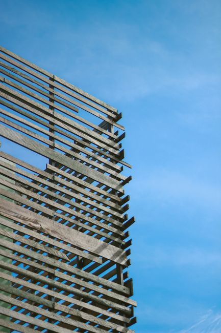 Minimalist wooden slat architecture contrasting with a clear blue sky, emphasizing modern design.